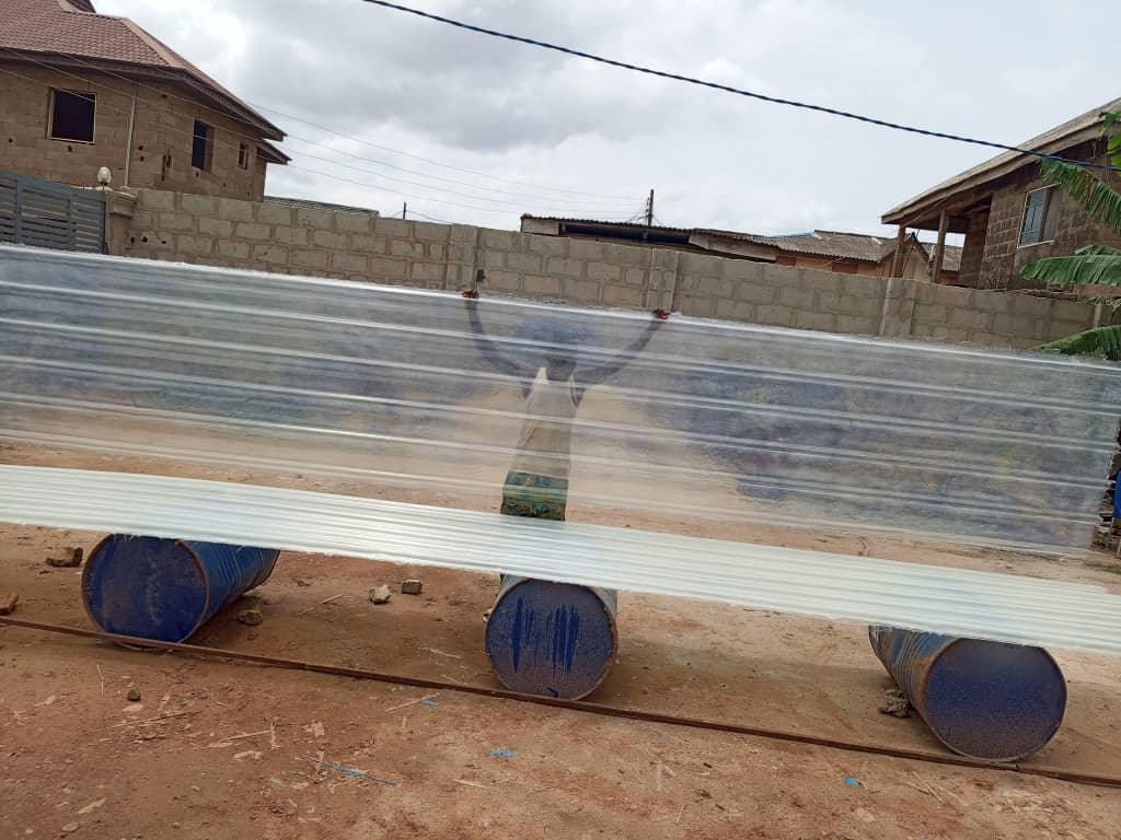 Clear transparent fibre glass roofing sheet held up outdoors, showing a person's silhouette through the material