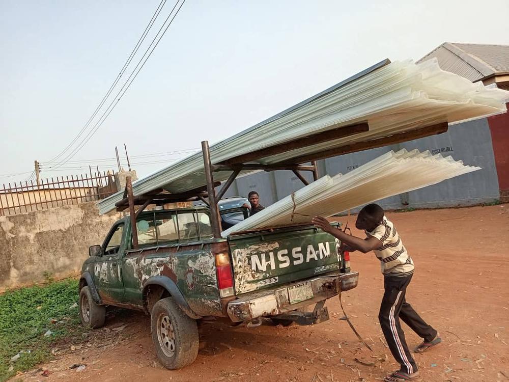 Workers loading Bestower fibre glass roofing sheets onto a pickup truck for delivery